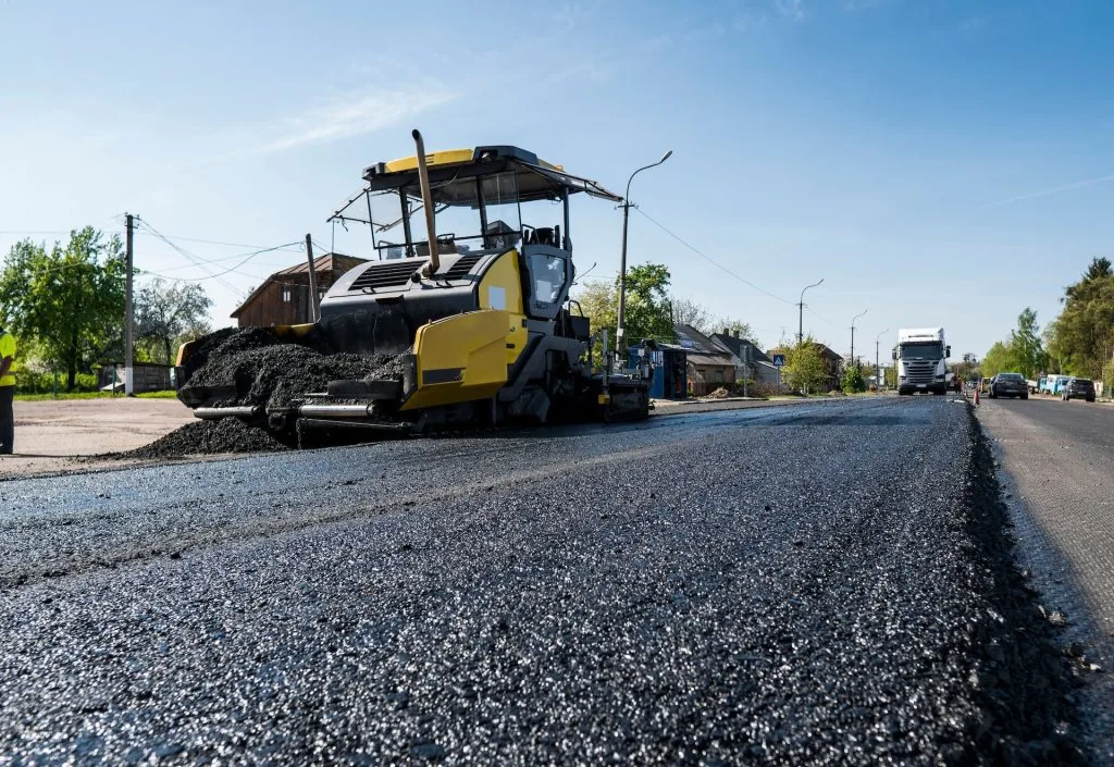 yellow asphalt paver on the side of a freshly paved road